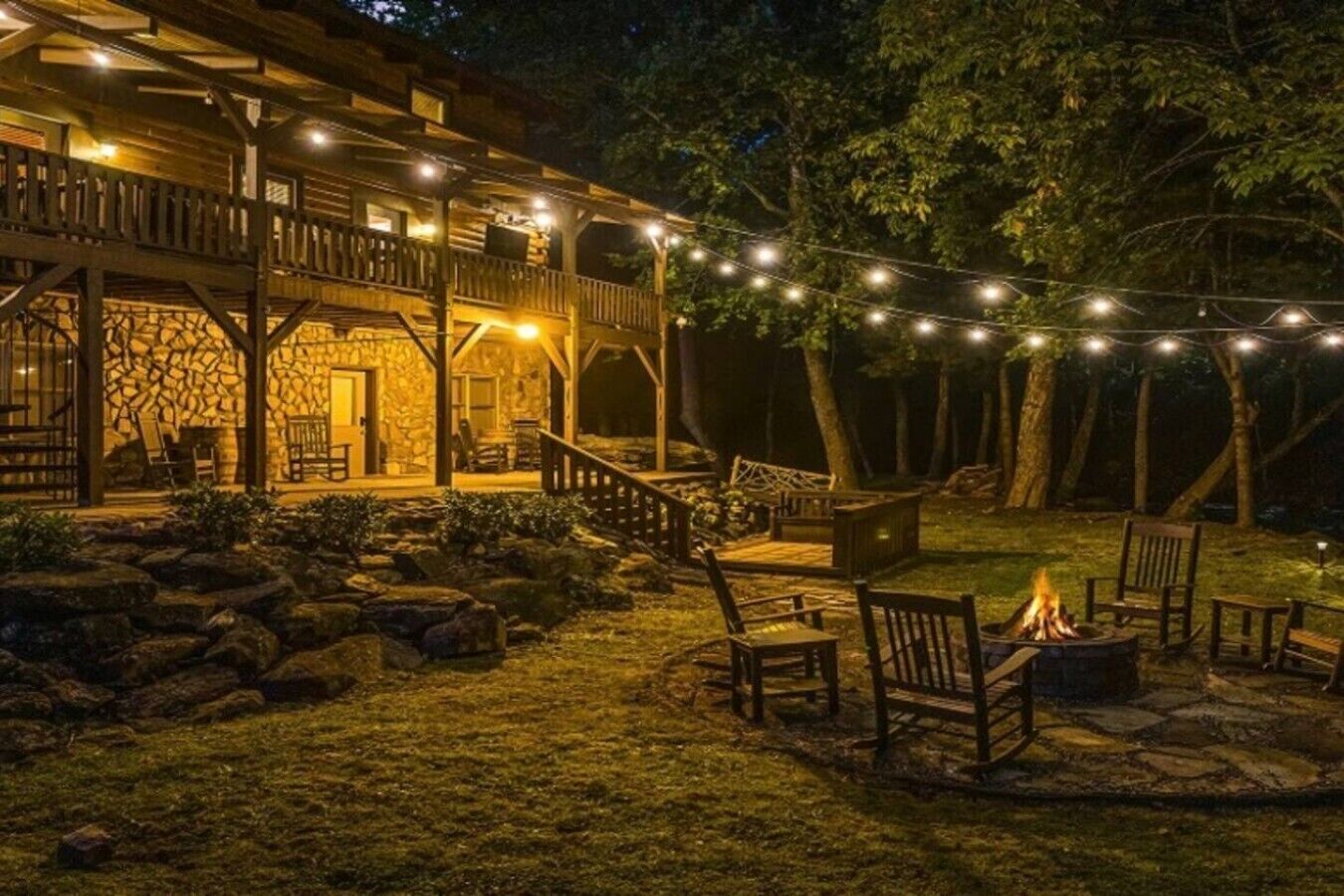 Une cabane en bois avec une façade en pierre, des sièges d’extérieur et des guirlandes lumineuses.