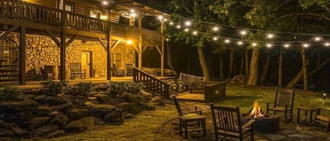 Una cabaña de madera con fachada de piedra, mobiliario exterior e iluminación con luces colgantes.