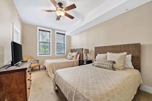 A bedroom with two beds, a ceiling fan, a TV, and a desk. - Kiva Village A 101 - Golf Course & Sunset Views Luxury 3BR Condo Near Fort Morgan Beach (Gulf Shores)