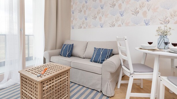 Una sala de estar con un sofá, una mesa de comedor con sillas, una mesita de madera y una ventana con cortinas translúcidas.