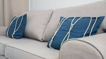 Un sofá color arena con dos almohadas azules con ribete de cuerda blanca.