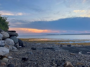 Kallioinen rantaviiva, josta avautuu näkymä vedelle ja auringonlaskuun.