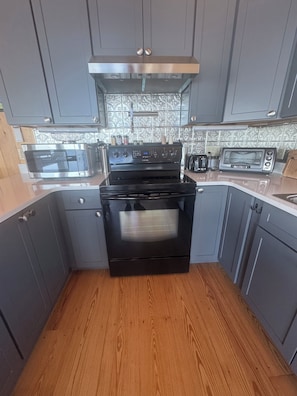 A kitchen with grey cabinets, a black stove, a microwave, and a toaster.