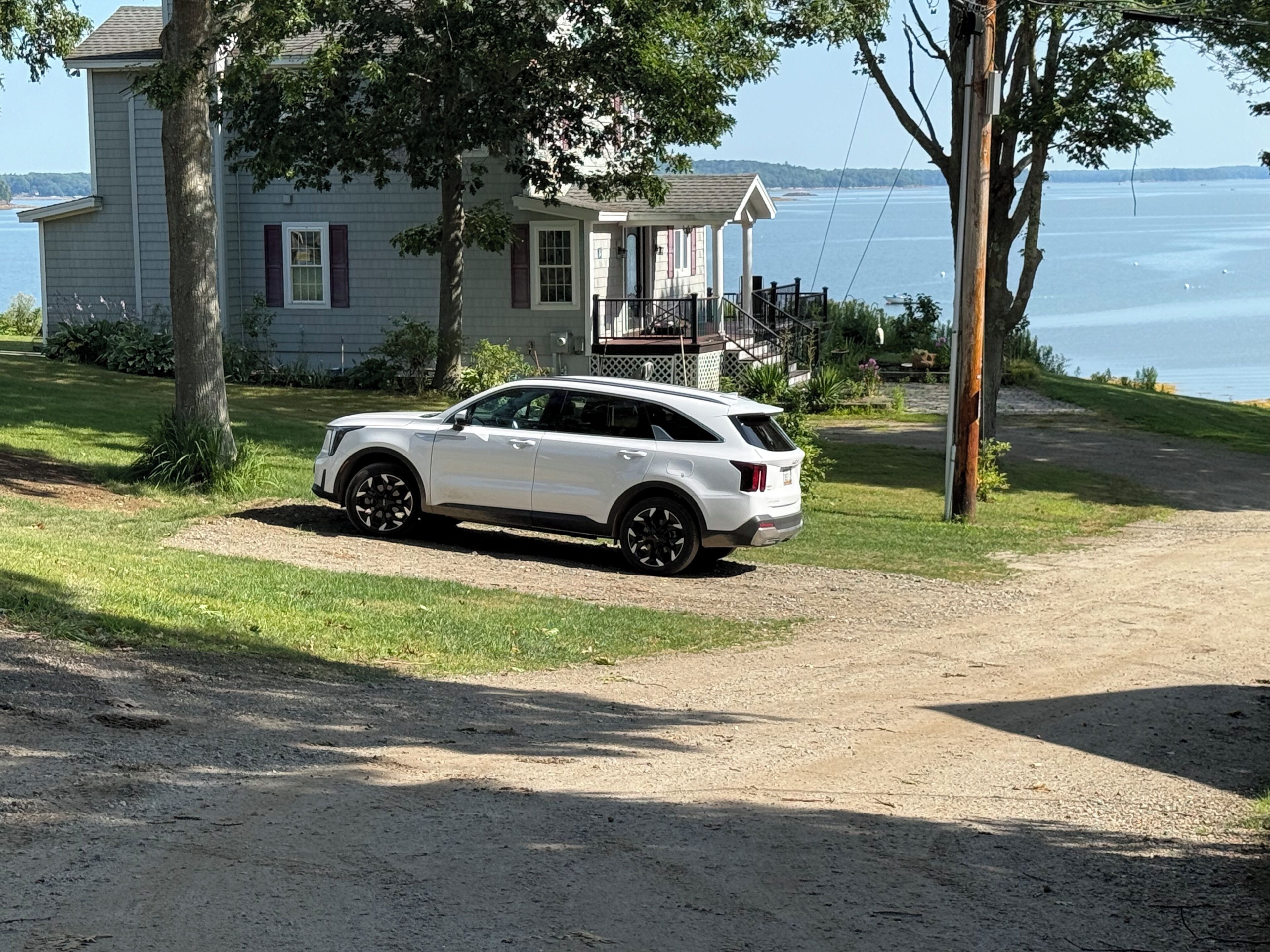 A white SUV parked on a gravel driveway in front of a house with a view of the water.