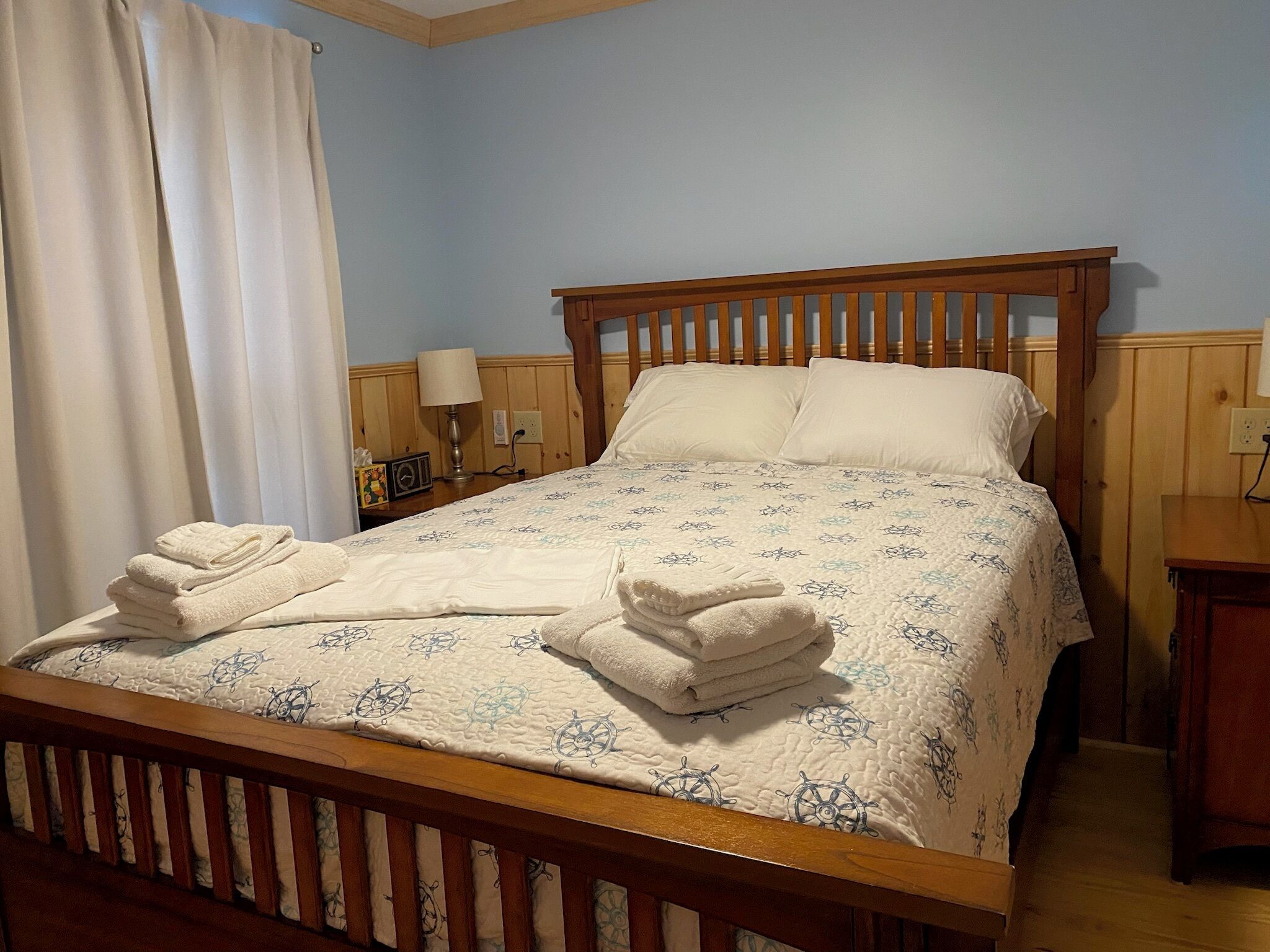 A neatly made bed with a patterned bedspread and two pillows, a bedside lamp, and a folded towel on the bed.