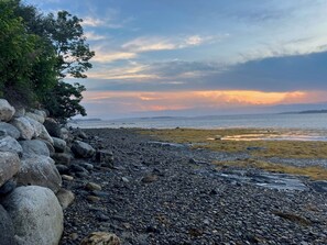 A rocky shoreline with a view of the sea and distant land under a cloudy sky.