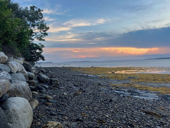 A rocky shoreline with a view of the sea and distant land under a cloudy sky.