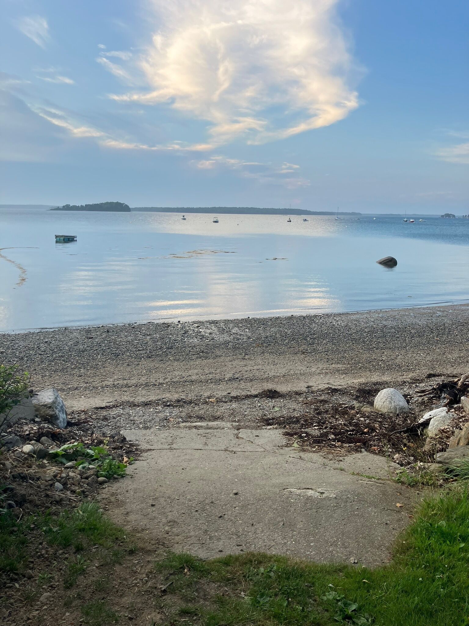 A pebbly beach with boats on the water and a distant island.