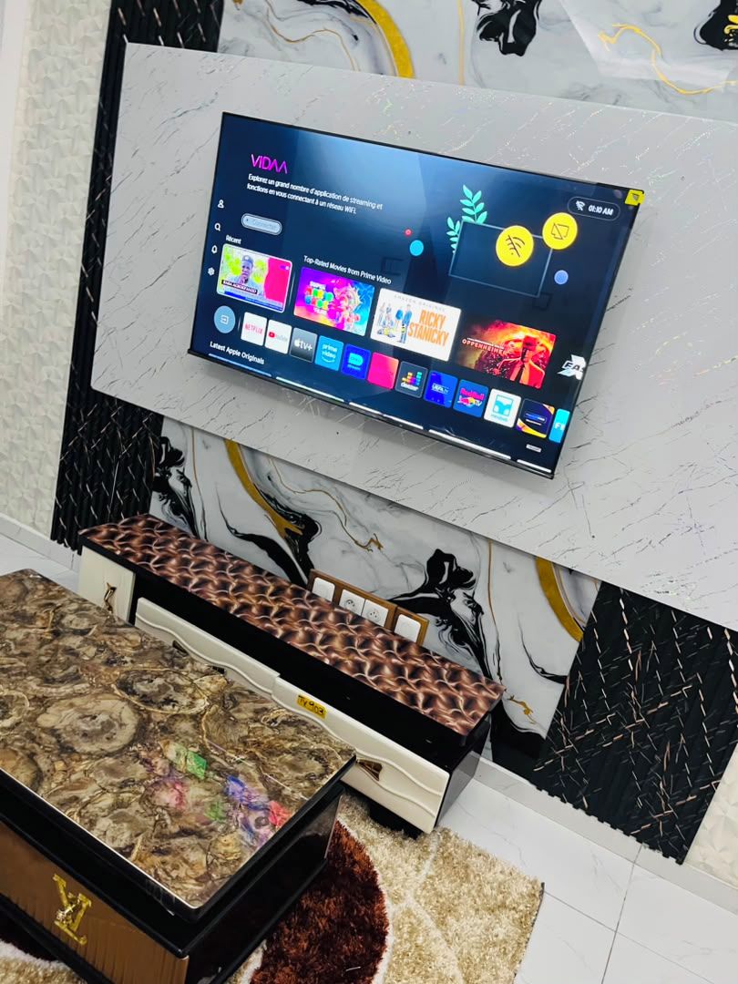 Un televisor de pantalla plana montado en una pared con diseño de mármol, un banco con cojín estampado y un adorno de pared.