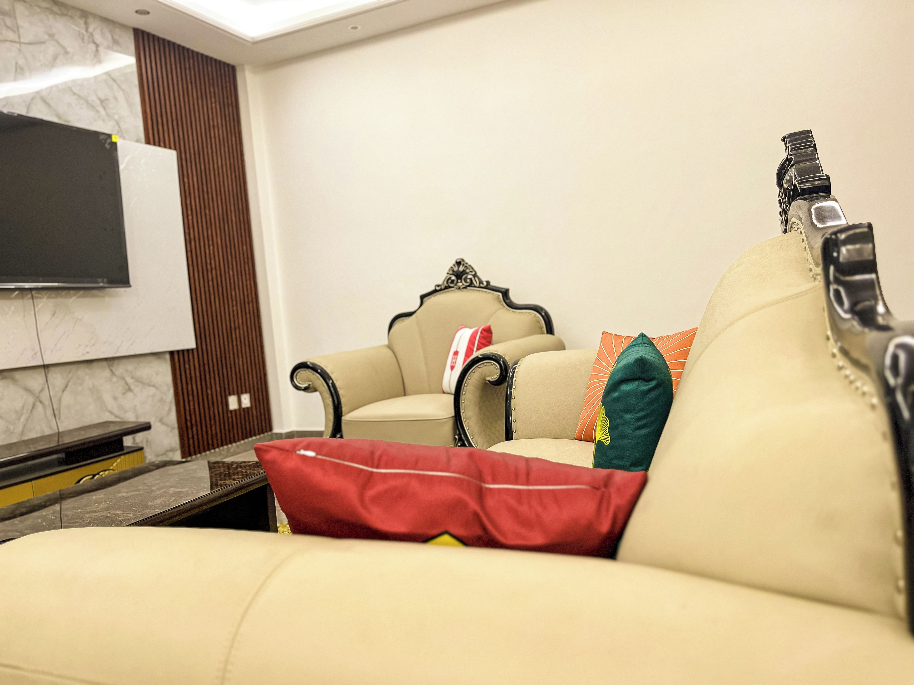 A living room with a sofa, two armchairs, and a flat-screen TV mounted on the wall.