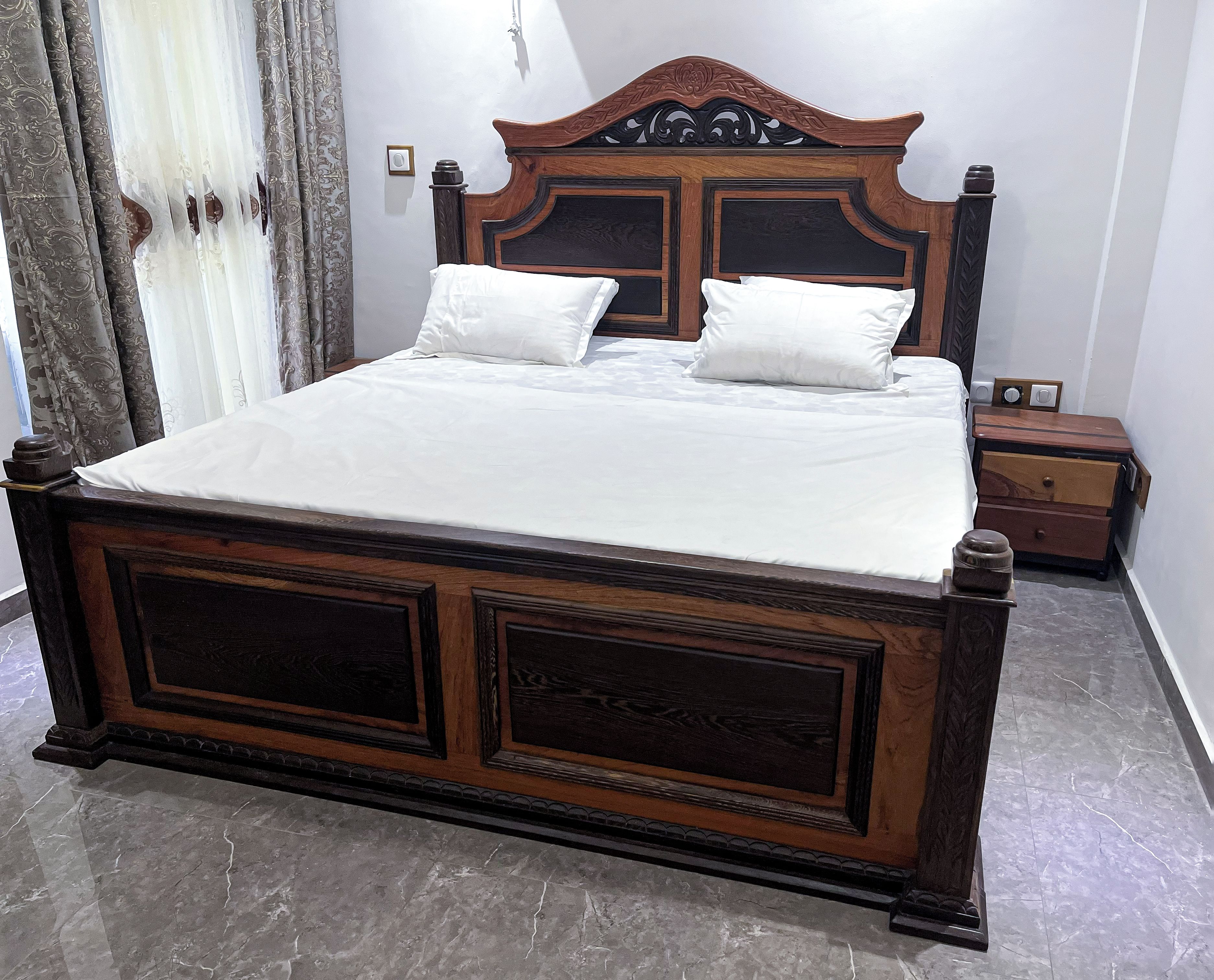 A bed with a wooden headboard and two pillows, a nightstand with a lamp, and a marble floor.