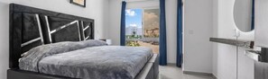 A bedroom with a bed, a nightstand, a window with curtains, and a view of the outside. - Casa Zoe Zafiro Residencial Sleeps 16 (San Vicente)