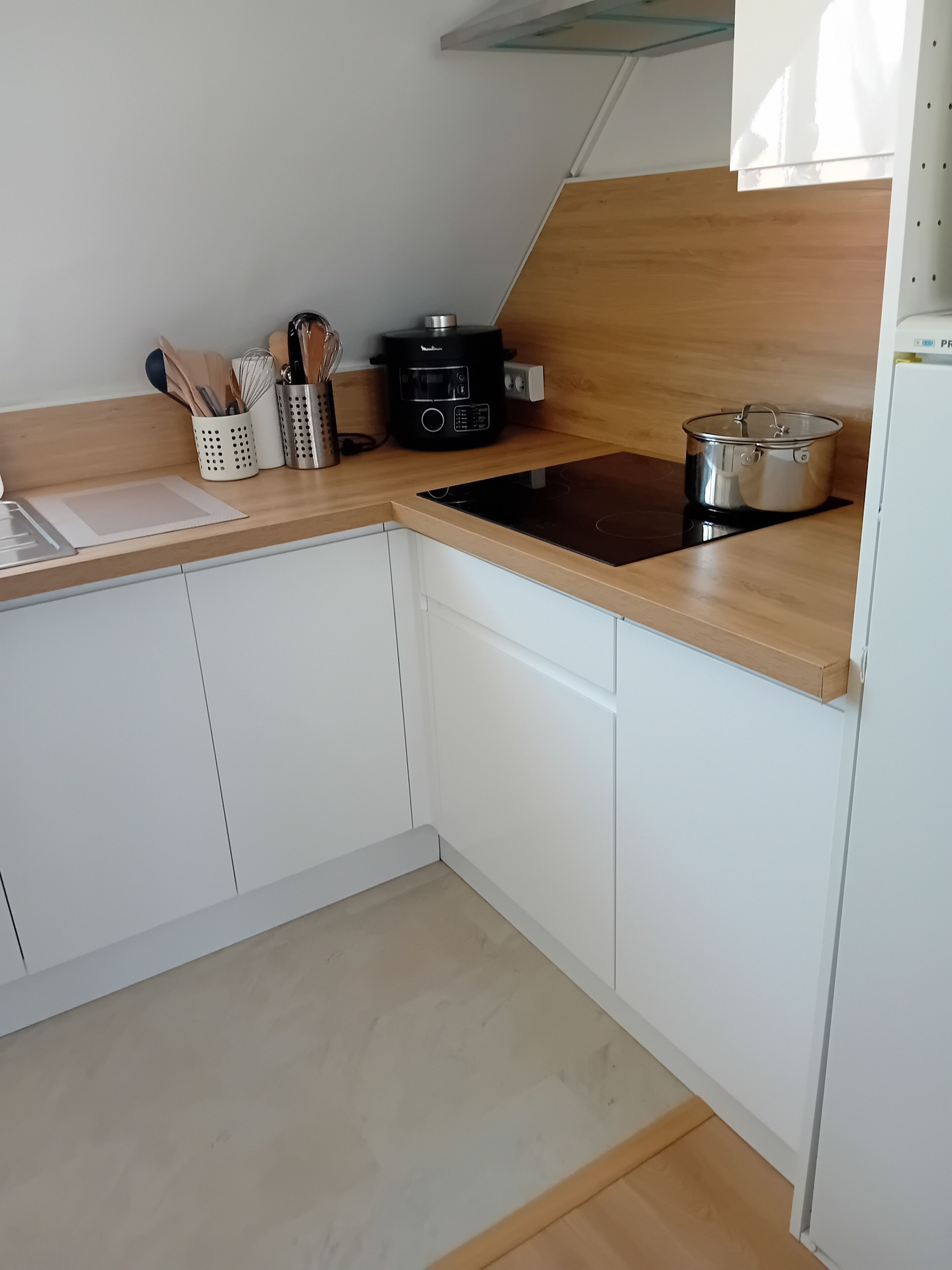 Une cuisine moderne avec des meubles blancs, une plaque de cuisson à induction noire, une casserole en acier inoxydable et une machine à café.