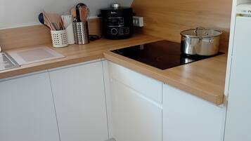 Une cuisine moderne avec des meubles blancs, une plaque de cuisson à induction noire, une casserole en acier inoxydable et une machine à café.