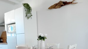 A white dining table with four chairs, a white vase with white flowers, and a white wall with a hanging plant and a mounted animal head.