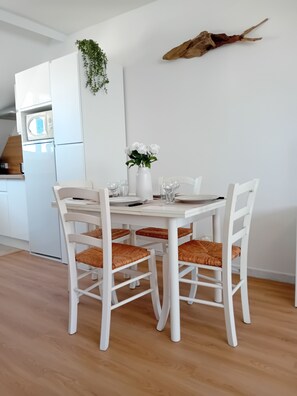 A white dining table with four chairs, a white vase with white flowers, and a white wall with a hanging plant and a mounted animal head.
