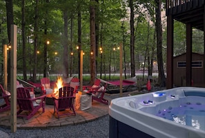 Un jacuzzi con una chimenea y sillones Adirondack rojos en un área boscosa al aire libre.