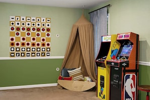 Ein Zimmer mit grüner Wand, einem Baldachinbett, einer Pac-Man-Spielmaschine und einem Schachbrett.