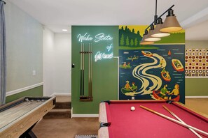Ein Billardtisch mit einer Neonreklame, einem Billardständer und einem Wandgemälde, das eine Flusslandschaft zeigt.