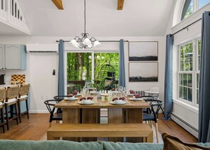 Ein Essbereich mit einem Holztisch, gedeckt für eine Mahlzeit, umgeben von Stühlen und Blick ins Grüne.
