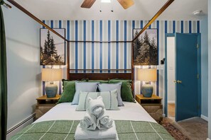 Ein Schlafzimmer mit einem Himmelbett, gestreifter Tapete, zwei Nachttischen mit Lampen und einer blauen Tür.