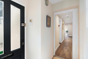 A hallway with a black door, a wall-mounted light fixture, and a framed welcome sign. - Coastal Calm | By My Getaways (Brighton)