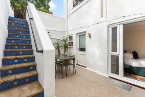 A staircase with blue mosaic tiles, a small outdoor table with chairs, and a sliding glass door leading to a bedroom. - Coastal Calm | By My Getaways (Brighton)