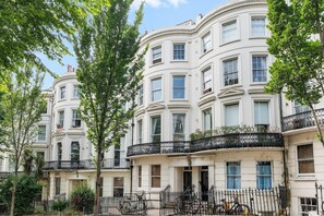 A row of white, multi-story buildings with balconies, surrounded by trees. - Coastal Calm | By My Getaways (Brighton)