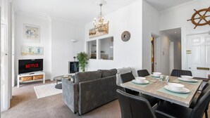 A modern living room with a TV, sofa, dining table, and chairs. - Seaview Haven | By My Getaways (Brighton)