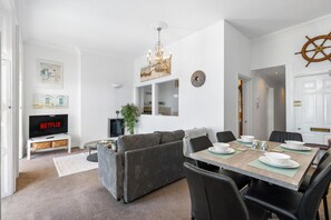 A modern living room with a TV, sofa, dining table, and chairs. - Seaview Haven | By My Getaways (Brighton)