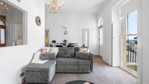 A living room with a grey sofa, ottoman, chandelier, and a large mirror. - Seaview Haven | By My Getaways (Brighton)