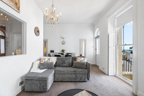 A living room with a grey sofa, ottoman, chandelier, and a large mirror. - Seaview Haven | By My Getaways (Brighton)