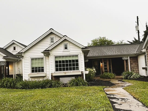 A two-story house with a front porch, a visible window, and a pathway leading to the entrance.