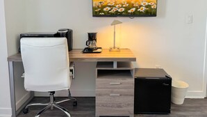 Ein modernes Büro mit Schreibtisch, Stuhl, Kaffeemaschine, Lampe und einem Fernseher, der eine Blumenwiese zeigt.