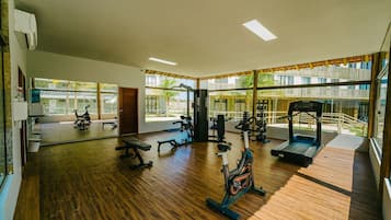 Uma academia com diversos equipamentos de exercício, amplas janelas e piso de madeira.