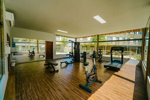 Uma academia com diversos equipamentos de exercício, amplas janelas e piso de madeira.