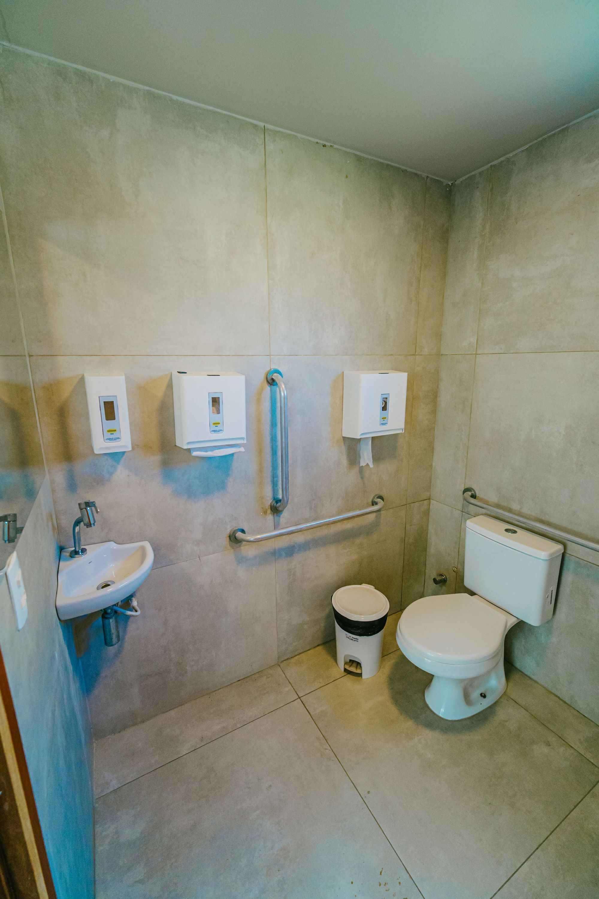 Et lille badeværelse med vask, toilet og to sæbedispensere på væggen.