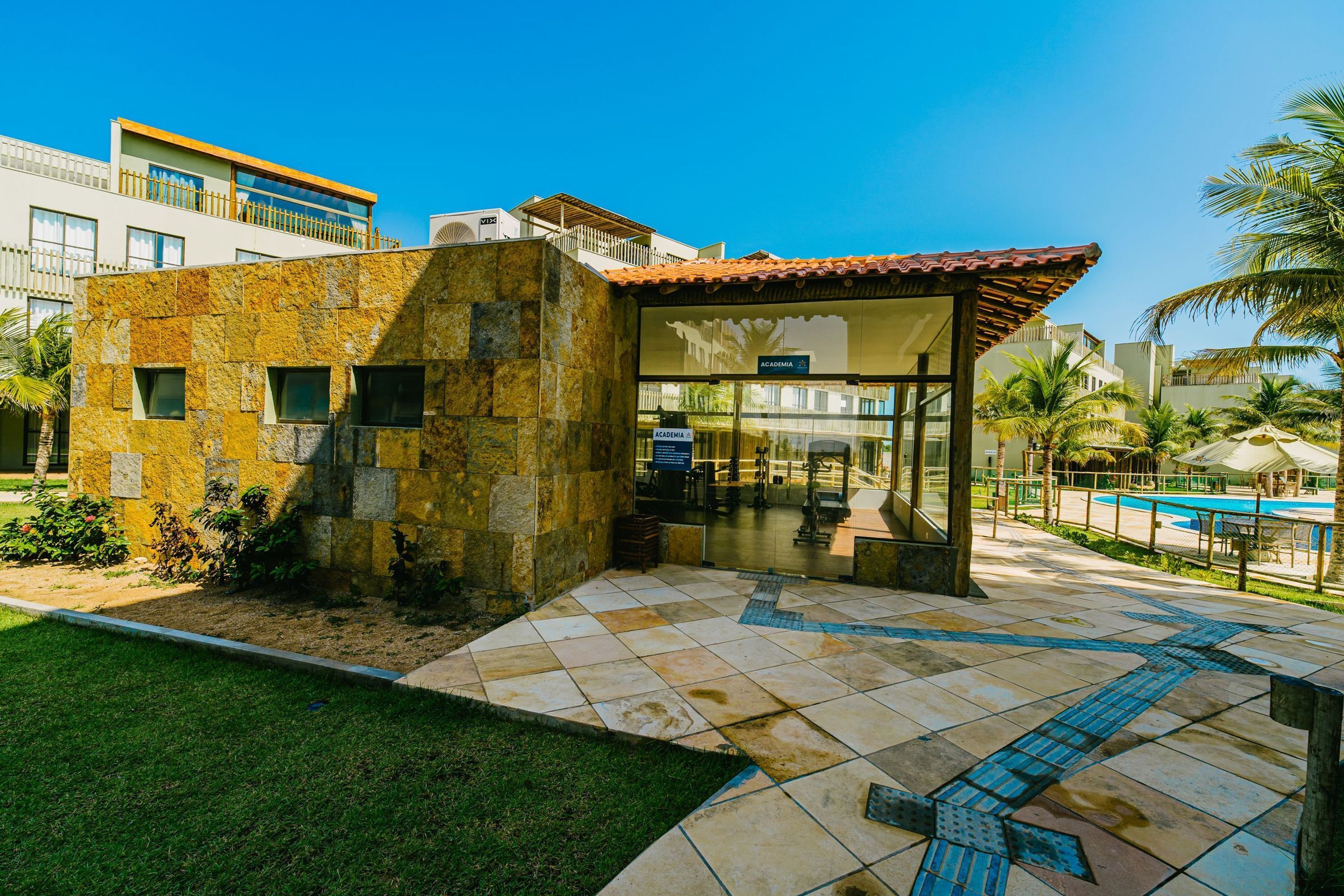 A modern building with a stone facade, a glass entrance, and a pool area.