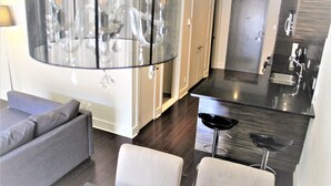 A modern living room with a grey sofa, a small table, and a bar area with a stool. - MODERN CONDO IN THE HEART OF DOWNTOWN FESTIVAL DISTRICT (Montréal)