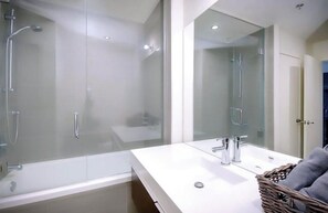 Ein modernes Badezimmer mit einer gläsernen Duschkabine, einem weißen Waschbecken mit zwei Wasserhähnen und einem Spiegel darüber.