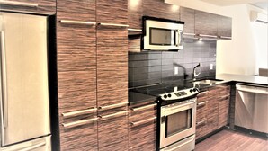 A modern kitchen with stainless steel appliances, dark wood cabinetry, and a black countertop. - MODERN CONDO IN THE HEART OF DOWNTOWN FESTIVAL DISTRICT (Montréal)