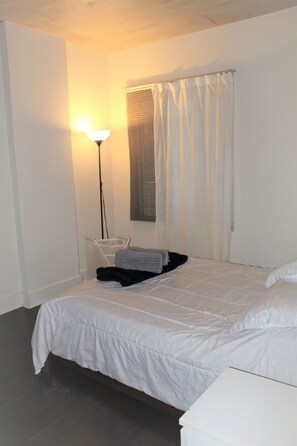 Ein Schlafzimmer mit Bett, Nachttisch, Lampe und einem Fenster mit Vorhängen.