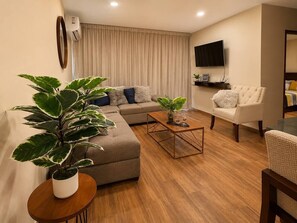 Een moderne woonkamer met een hoekbank, een salontafel en een potplant.
