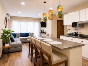 A modern kitchen with a central island, white cabinets, and a flat-screen TV mounted on the wall. - En el corazón de marina Mazatlán (Mazatlán)