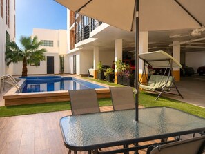 A pool area with a glass table and chairs, a swing chair, and a red vehicle in the background. - En el corazón de marina Mazatlán (Mazatlán)