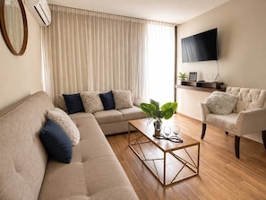 A living room with a sofa, armchair, coffee table, and a TV mounted on the wall. - En el corazón de marina Mazatlán (Mazatlán)