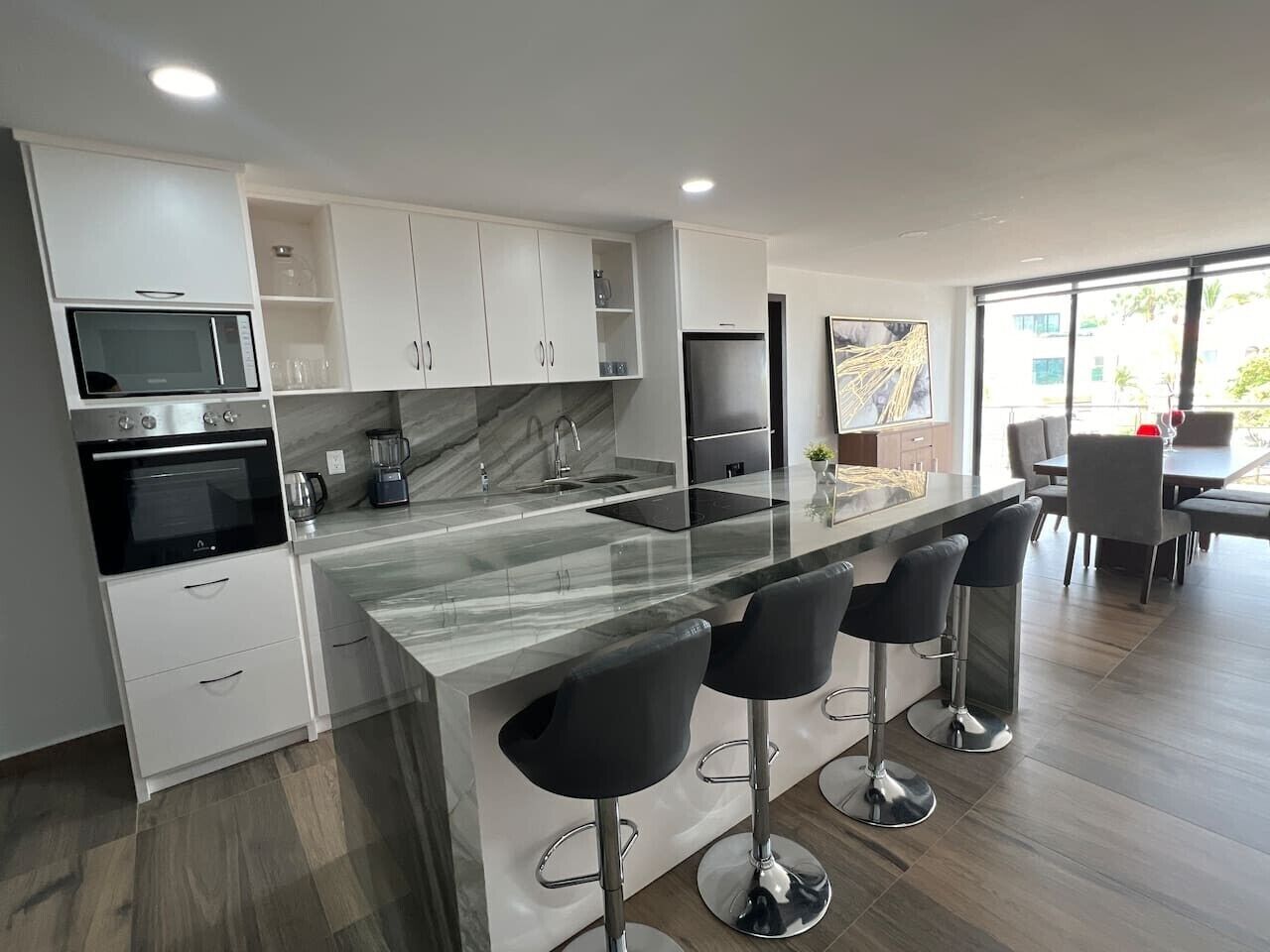 A modern kitchen with a central island, bar stools, and a dining area with a table and chairs.