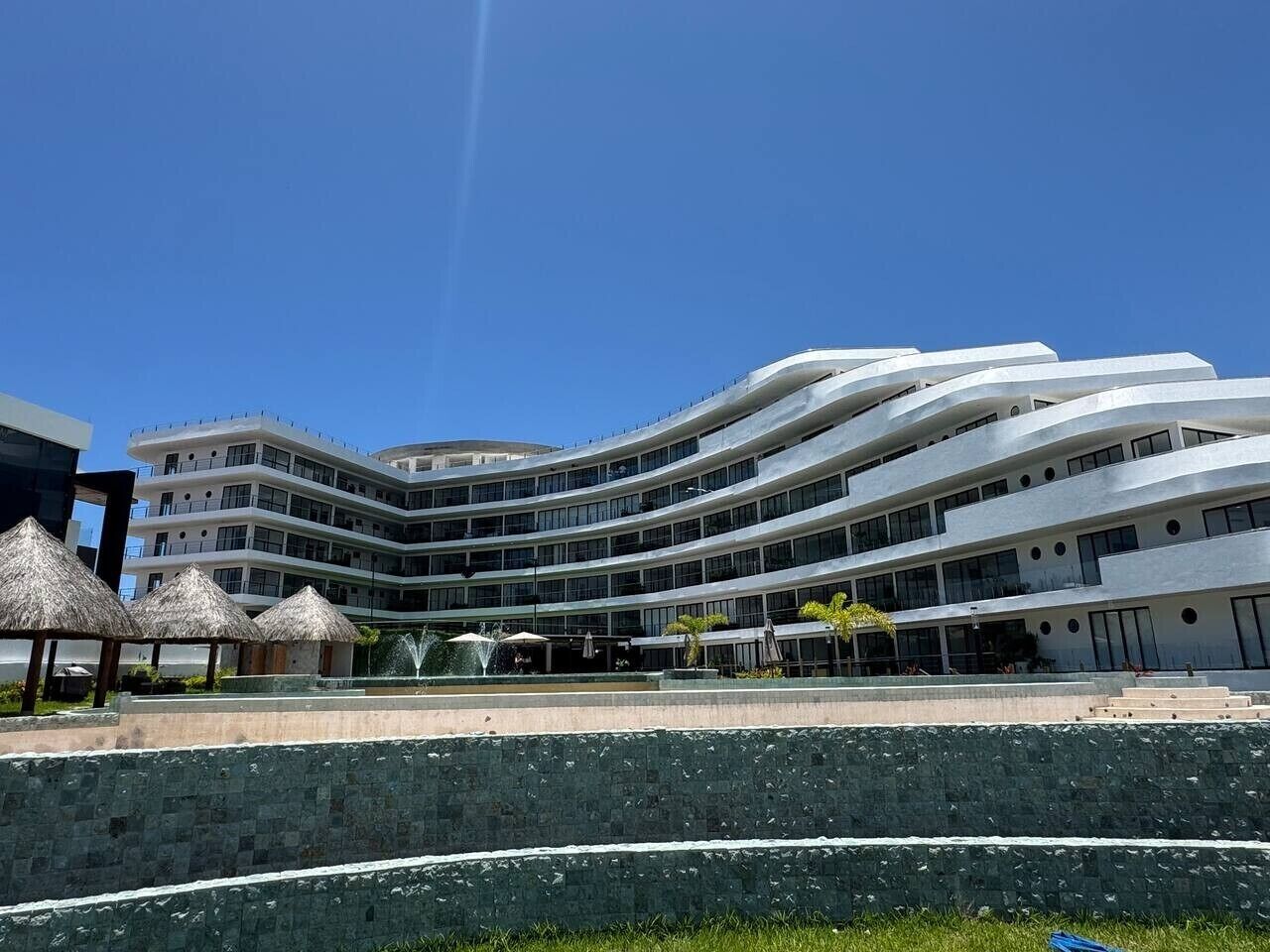 A modern hotel with a curved facade, multiple balconies, and a central courtyard with a fountain.