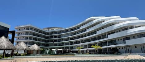 A modern hotel with a curved facade, multiple balconies, and a central courtyard with a fountain.
