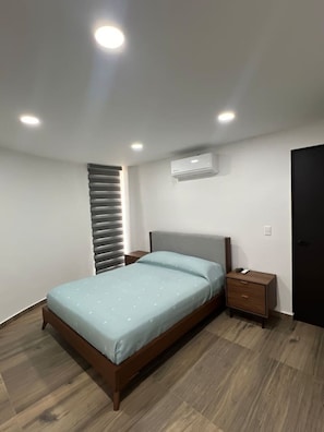 Ein Schlafzimmer mit Bett, Nachttischen, einer Klimaanlage und einem Fenster mit Jalousien.